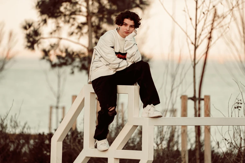 a boy sitting on top of a wooden bench next to a forest