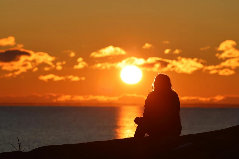 a person standing and sitting watching the sun go down