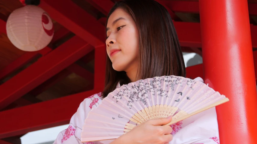 a woman in pink holding a fan near red pillars