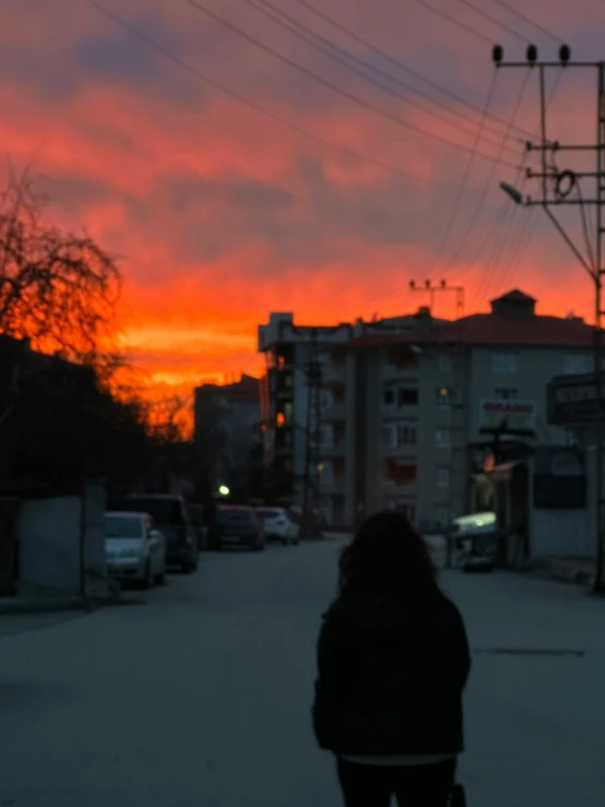 a person in winter clothing walking down a street under a sunset