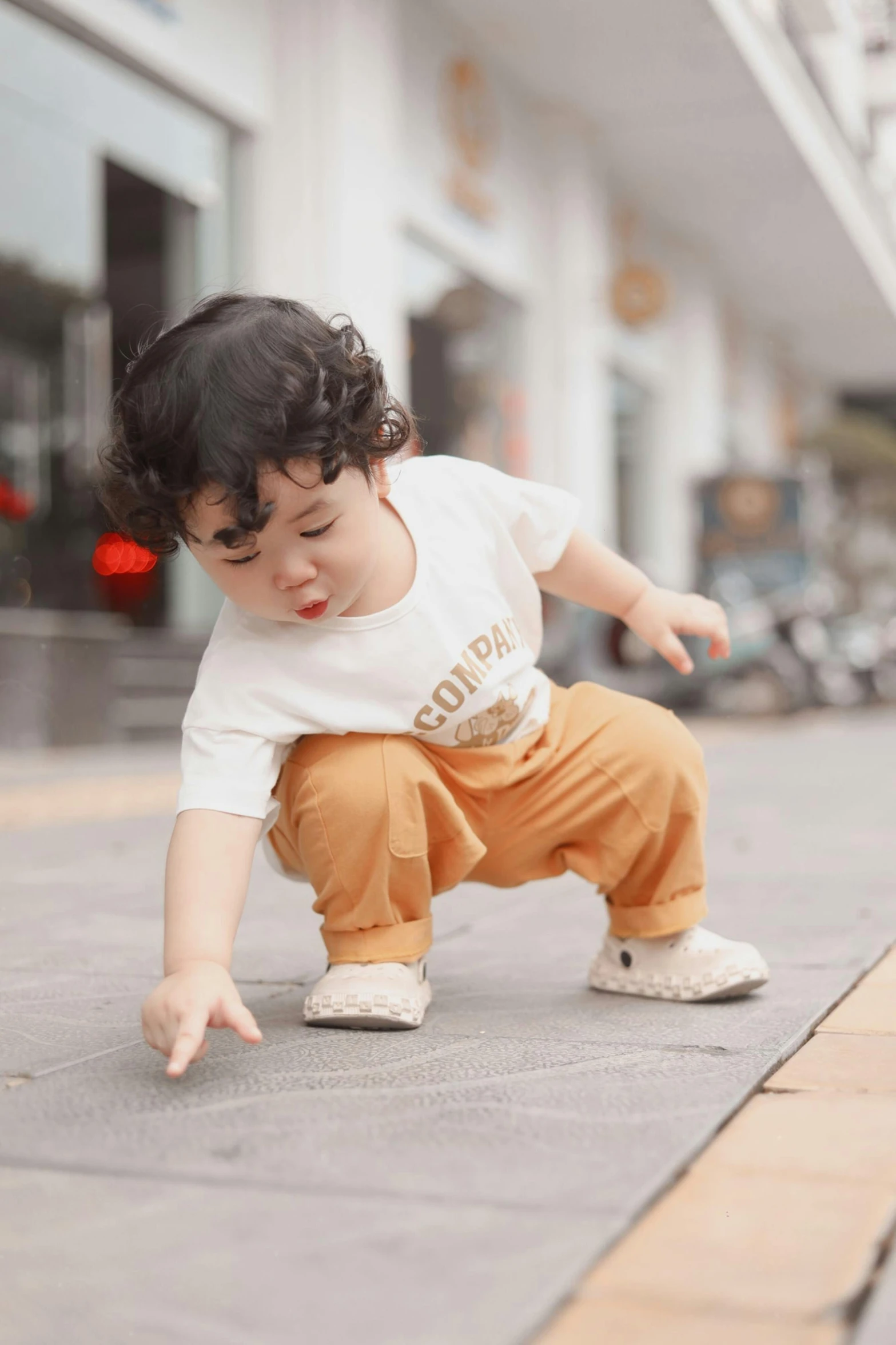 a baby boy dressed in an orange and white outfit leans forward on the ground