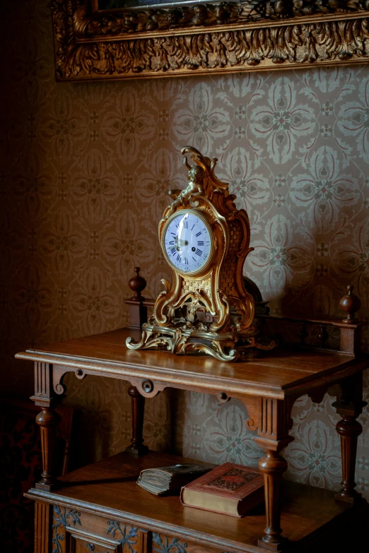 the small clock is gold in color against the brown wall paper