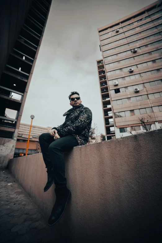 a man sitting on a wall and wearing sunglasses