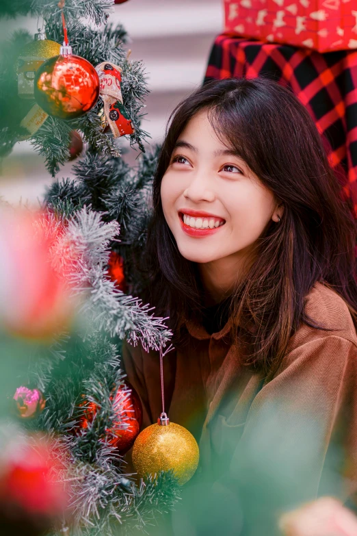 an asian girl is peeking out from behind a christmas tree