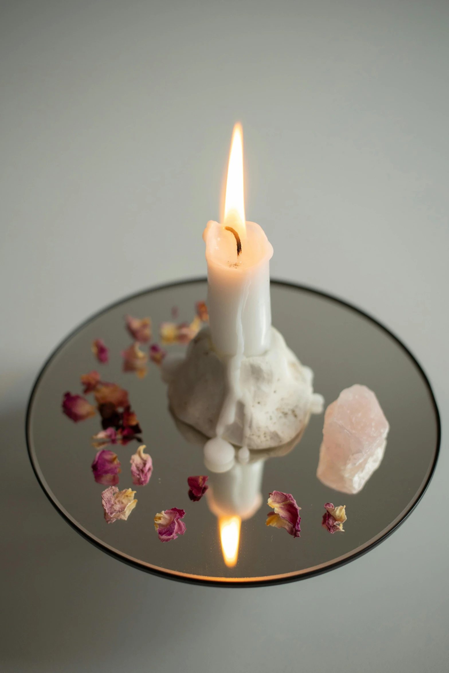 white candle is surrounded by rocks and petals