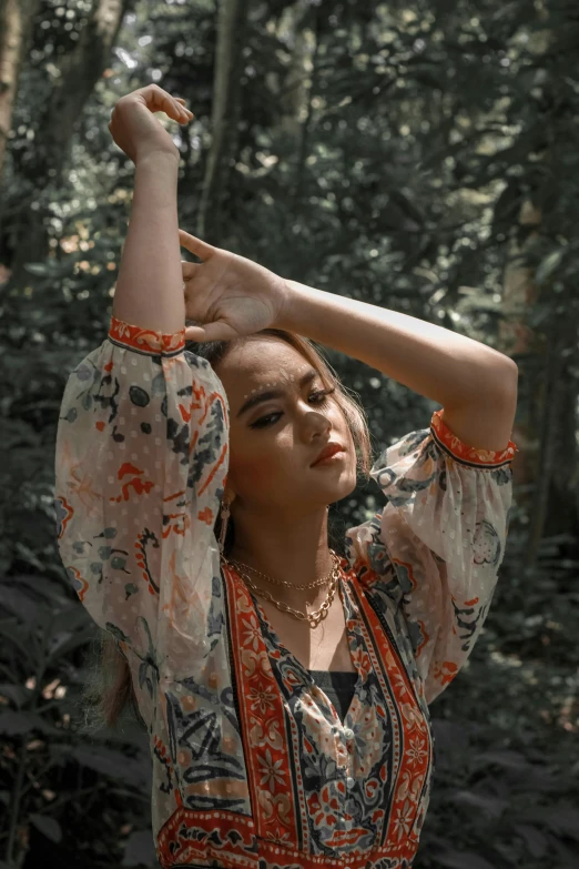 a woman standing in a forest while holding onto her hair