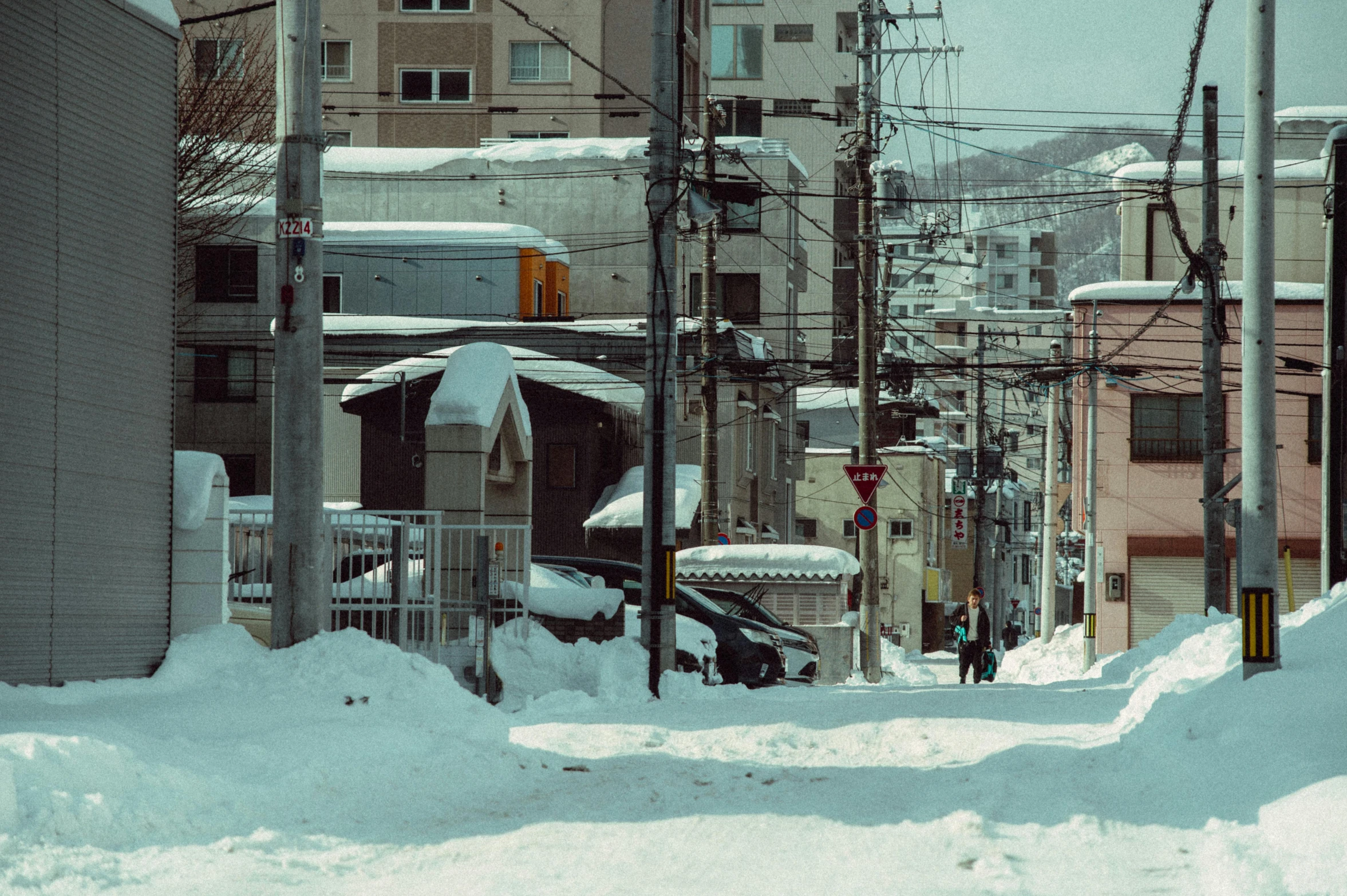 people walk through the snowy street near large buildings