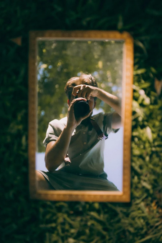 a man holding a camera in front of his face as seen through a mirror