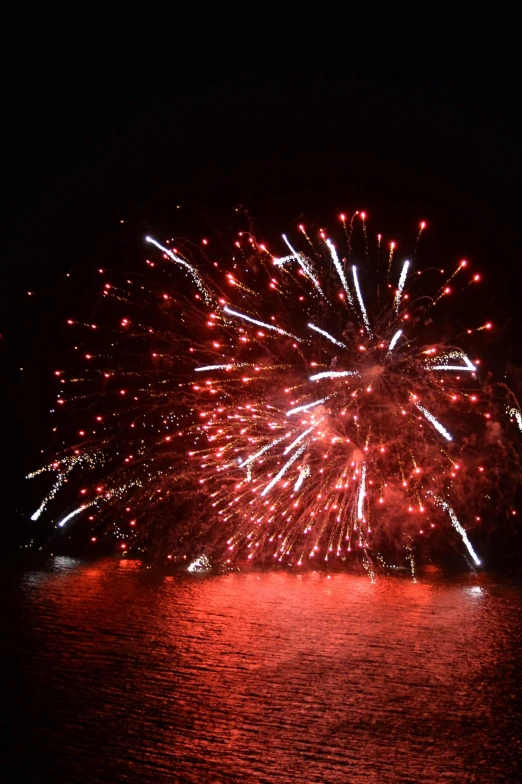 fireworks are lit up on the water while lights are reflecting in the dark