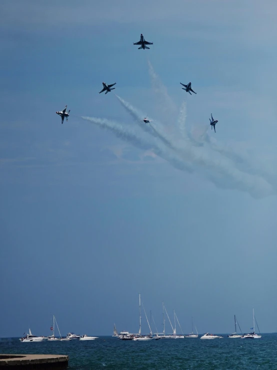 a group of planes flying over the ocean with yachts nearby