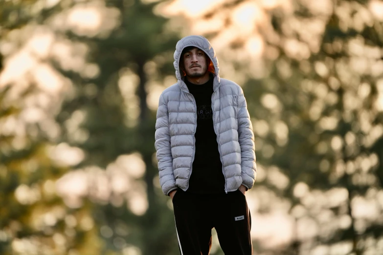 a man standing in front of some trees wearing a hoodie