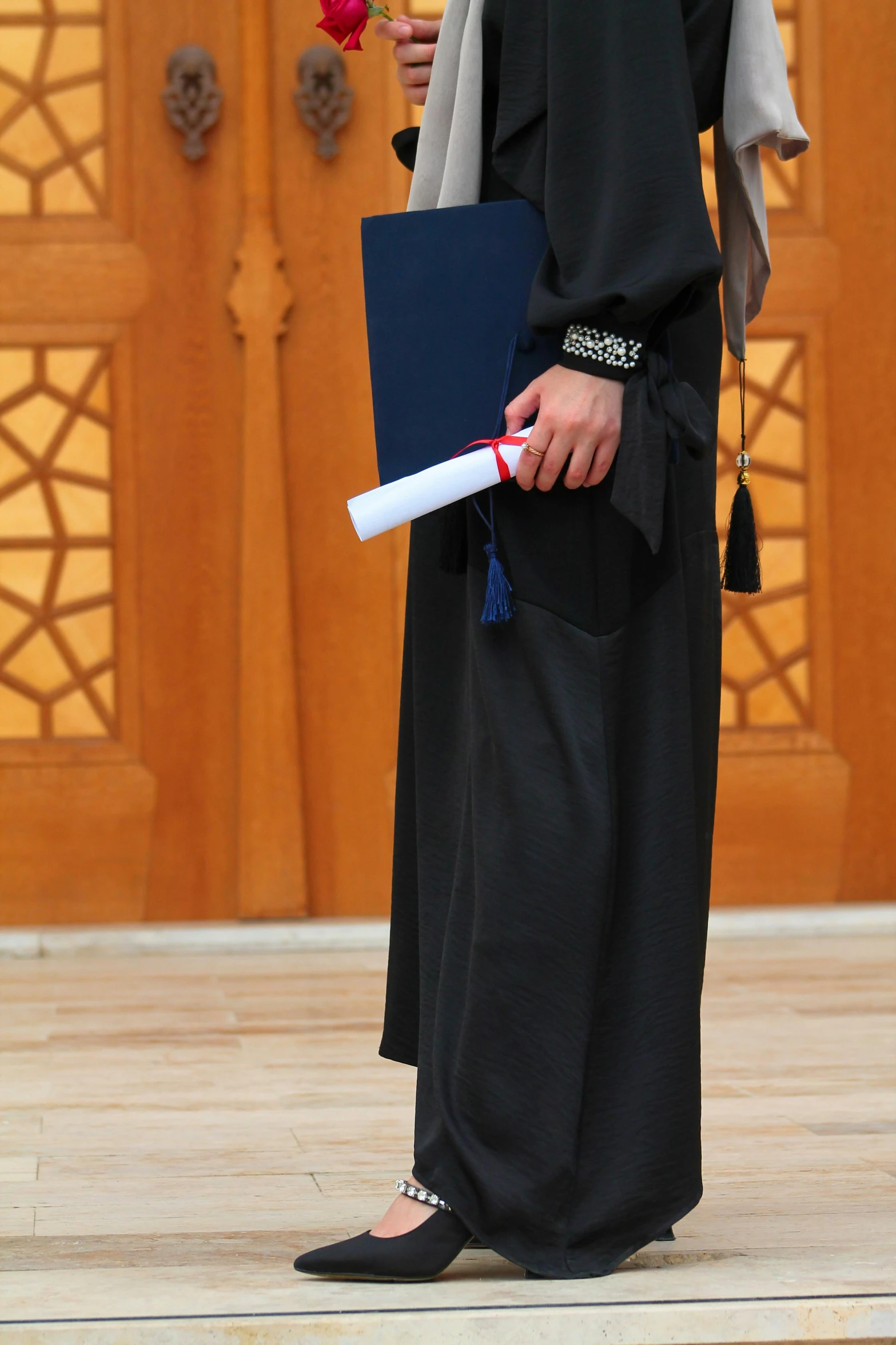 man with black robe holding a large blue book and holding flower