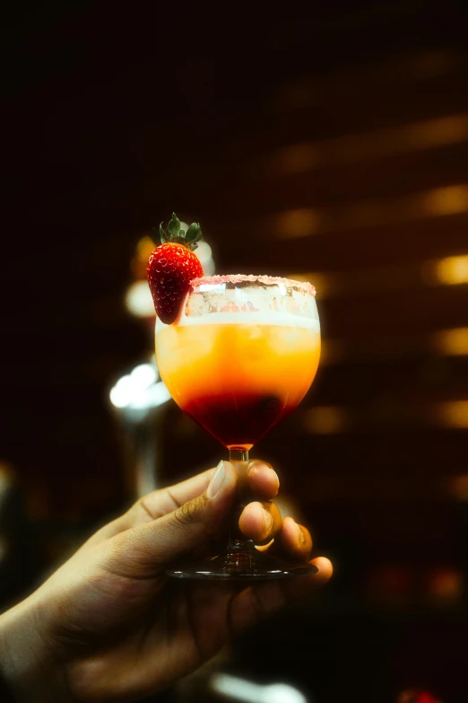 a person holding a glass with a red drink and strawberries