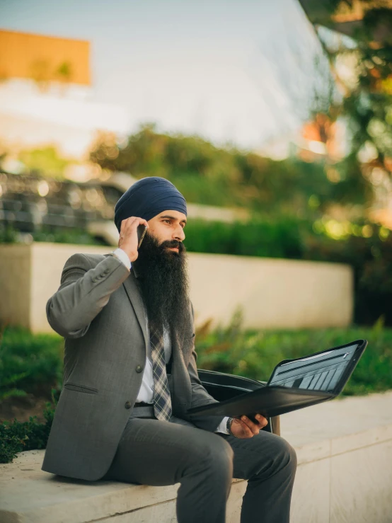 man in a turban and beard holding up his laptop