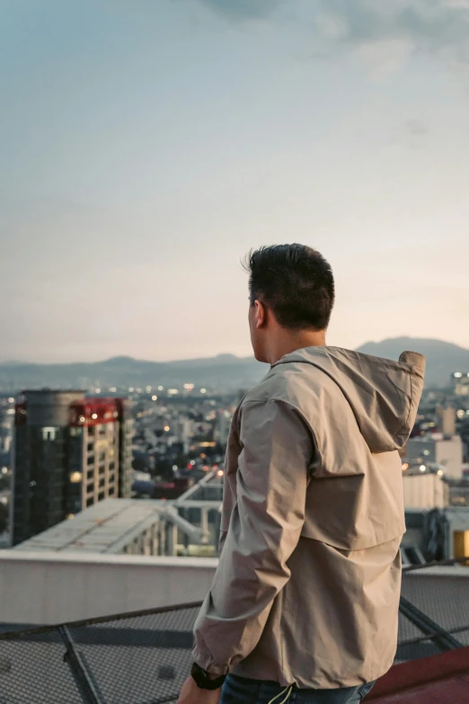 a man wearing a sweatshirt stands looking at a city