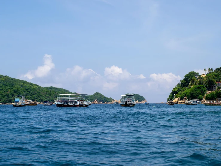 a few ships floating in the ocean with mountains and trees in the background