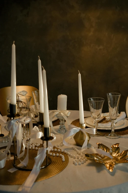 a dinner table with white dishes, gold candles, and ribboned linens