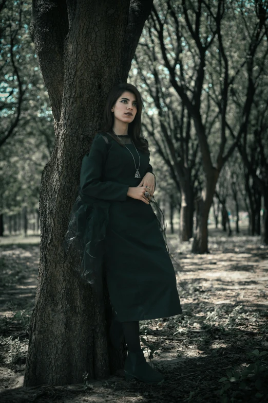 a woman posing for a po behind a tree in the middle of a park