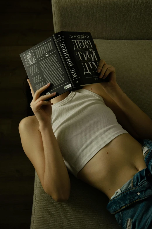 a young person laying on top of a green couch holding an open book