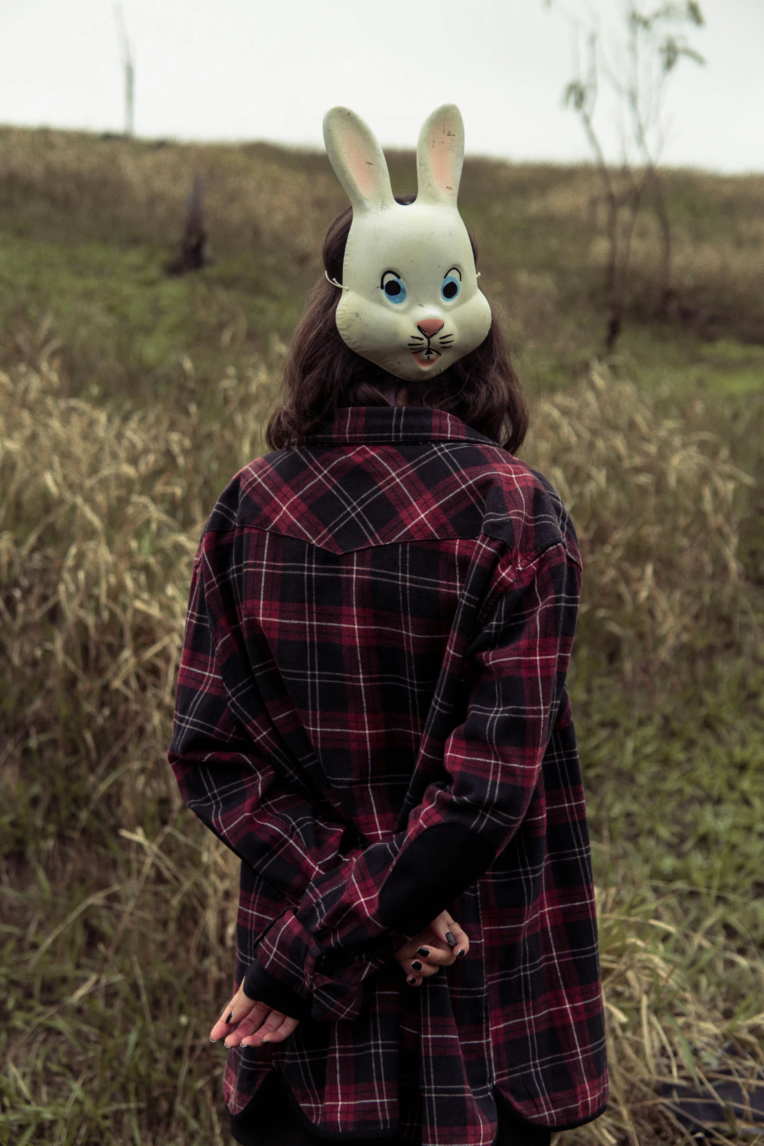 a woman with a rabbit mask is standing in a field