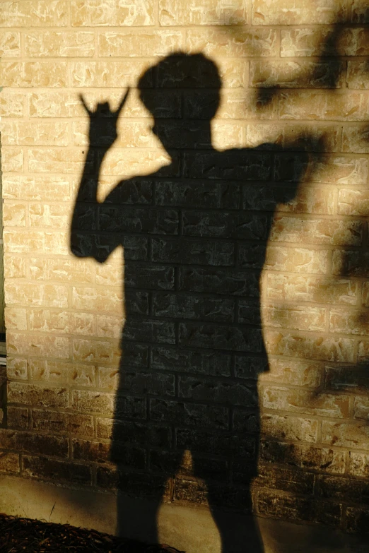 the shadow of a child with hat is making the peace sign