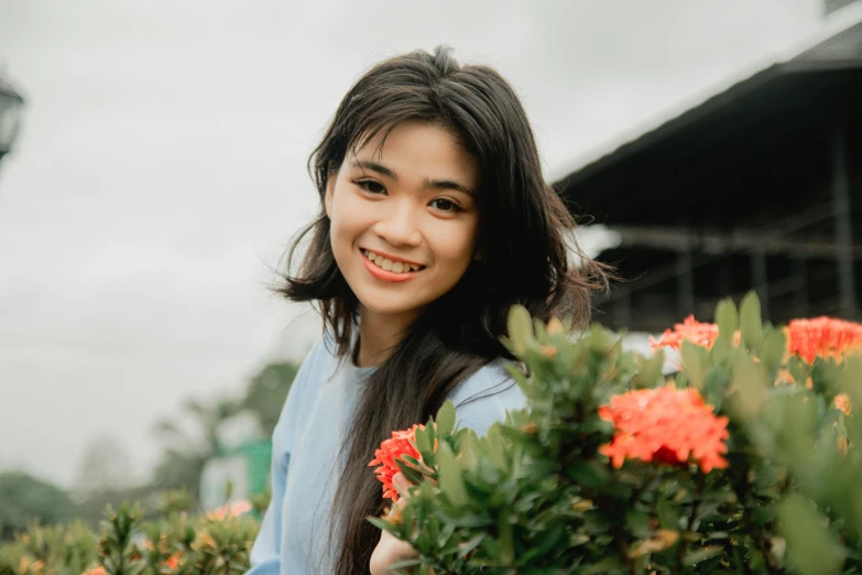 a young woman standing next to flowers, with sky in the background