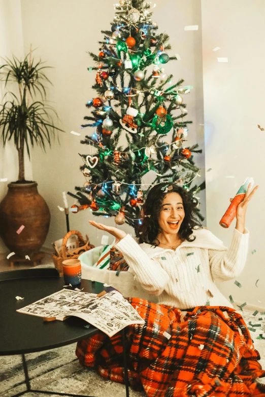 a woman is sitting on the floor with a christmas tree in front of her