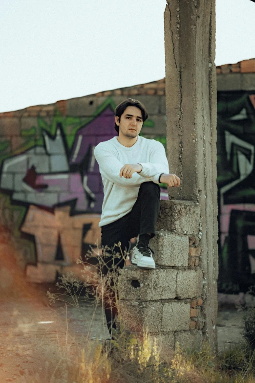 a man sits on a pillar covered in graffiti