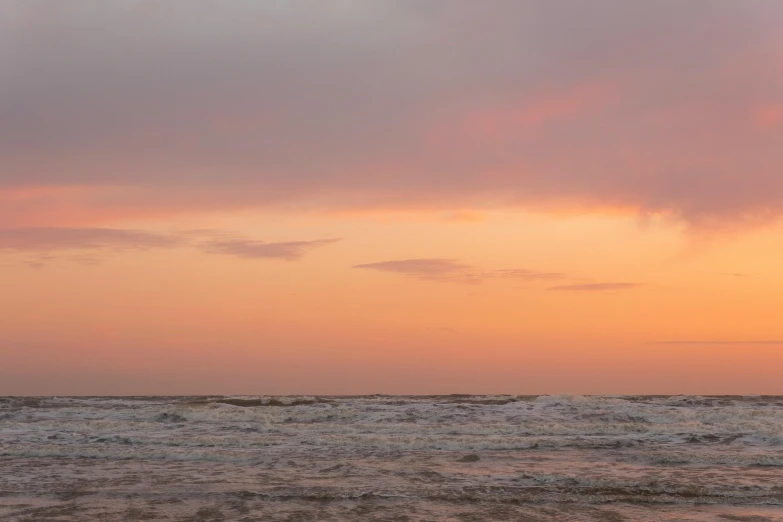 an surfer carrying his board into the ocean at sunset