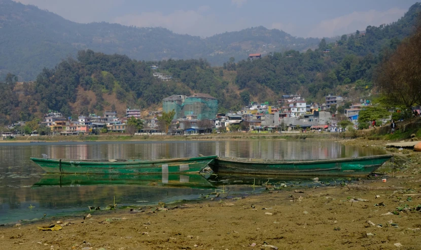 two green boats parked at the shore of a river