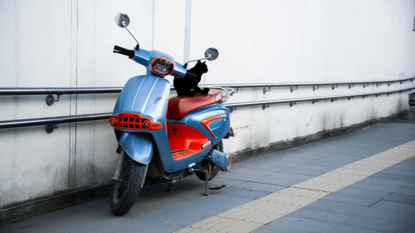 an orange and blue motor scooter sits in front of a wall