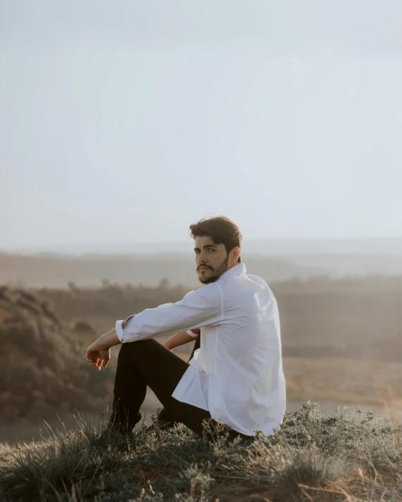 the man sits on a hill and poses for a pograph