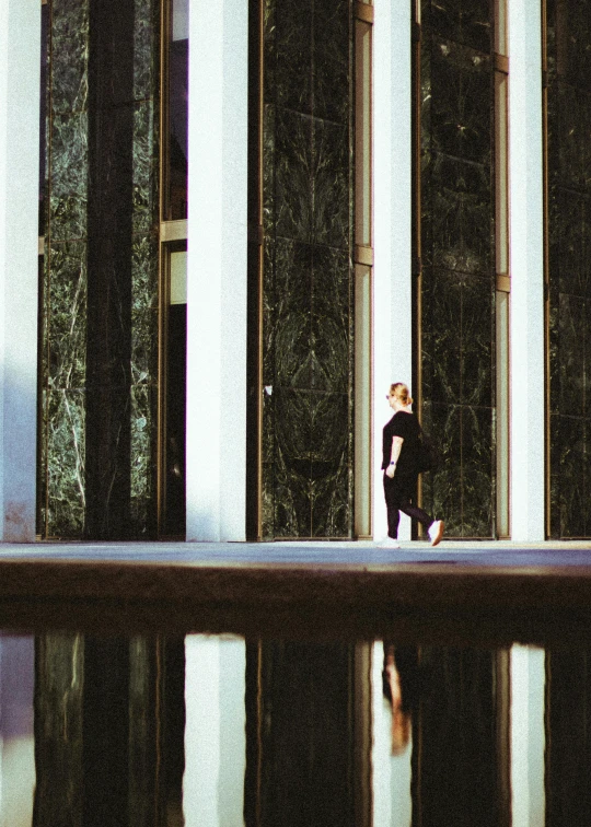 a person walks past tall columns with reflective water