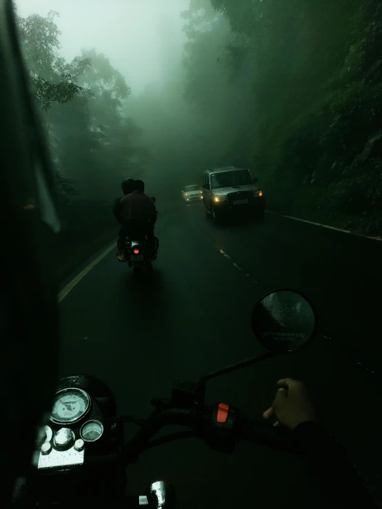 dark po of a motorcycle with headlights on while traffic travels on the road