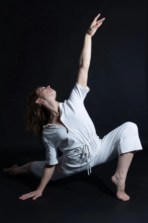 a woman in a white top on her stomach and arms outstretched, stretching on a black floor