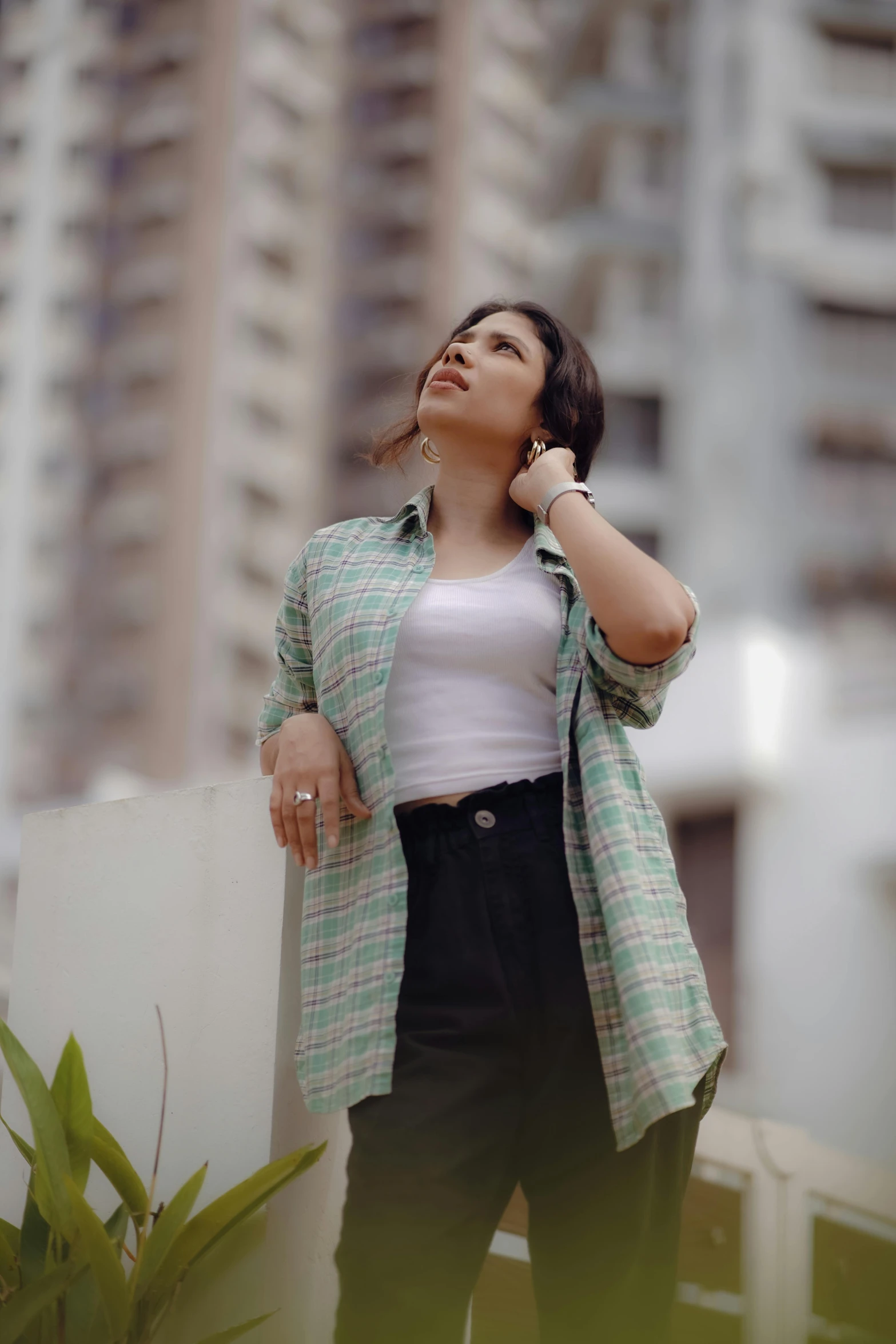 a woman in a green and white plaid jacket and black pants stands against a wall with one hand on her hips