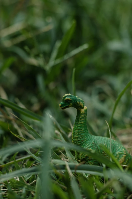 green toy dinosaur in the grass with a black beak