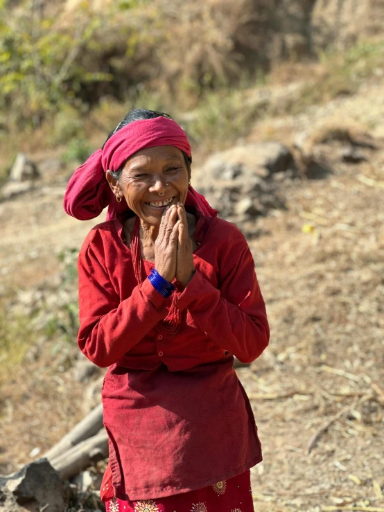 an old woman in a red outfit standing on the side of a dirt hill