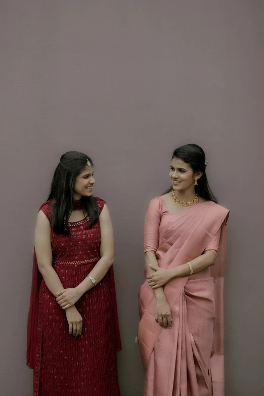 two women standing next to each other, in front of a wall