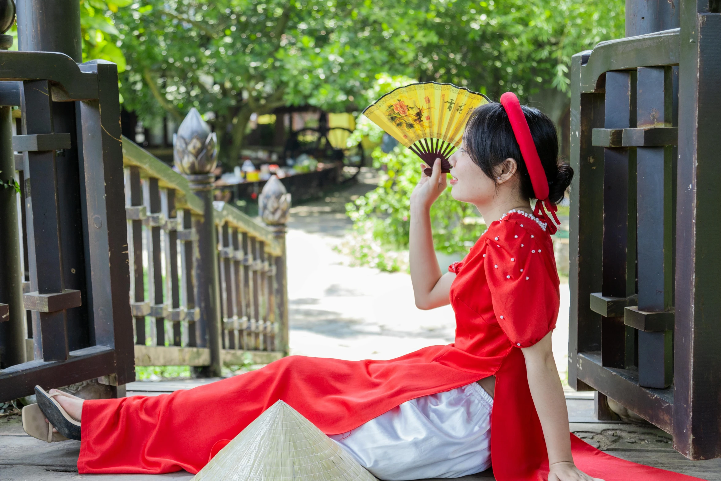 woman in red dress sitting on the ground holding a yellow fan