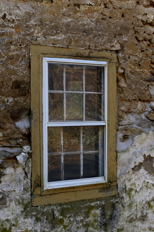 an old, peeling, dirty window sitting next to a rock wall