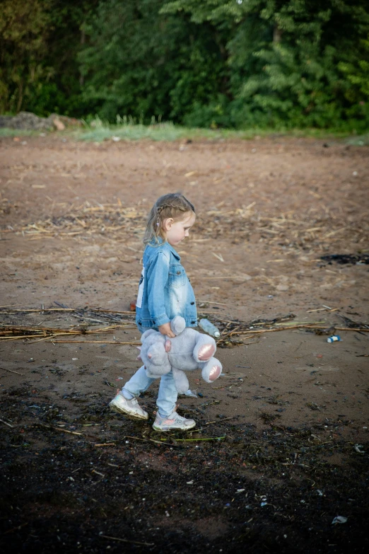 a small girl walks along a dusty field with trees in the background