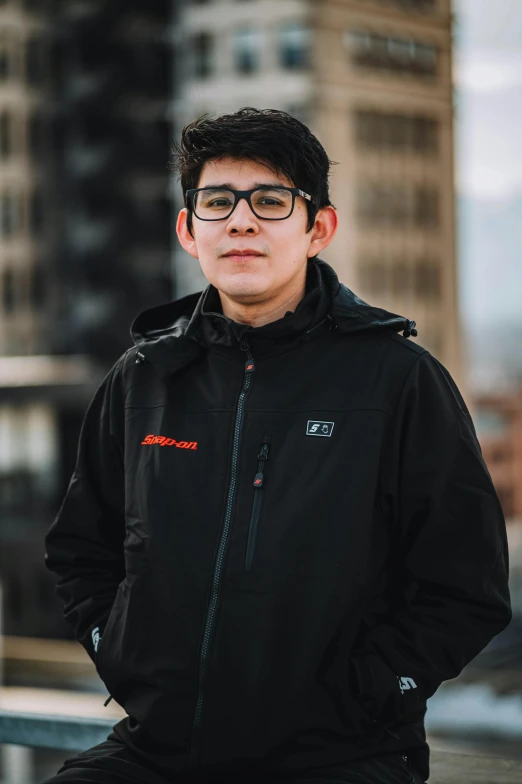 a man wearing glasses and standing in front of tall buildings