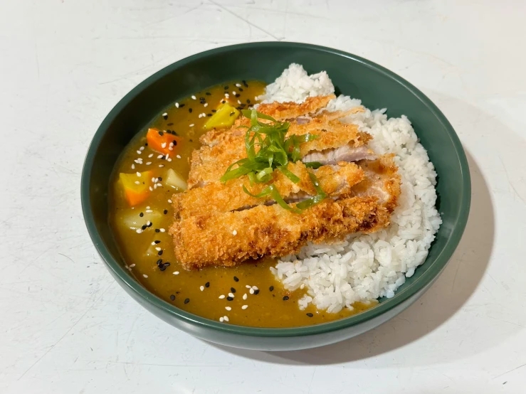 a dish in a green bowl filled with rice, vegetables and a fish