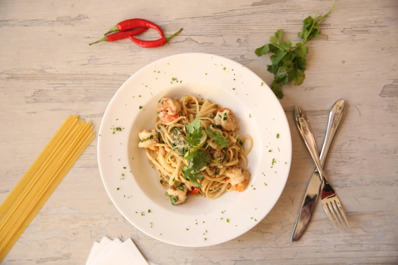 a white bowl full of food sitting on a table next to some silverware and forks