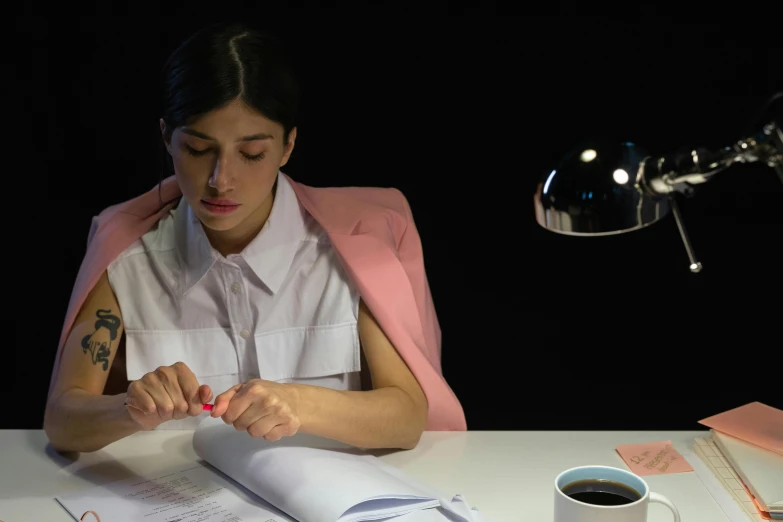 a woman sitting at a desk with an open book and a pen in her hands