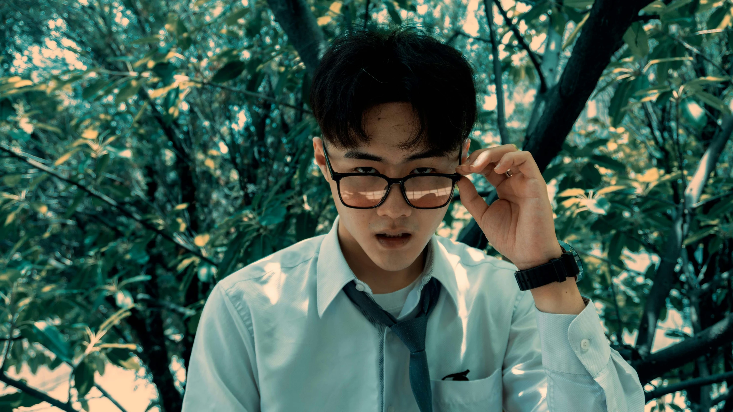 a young man with glasses holding his tie to his face