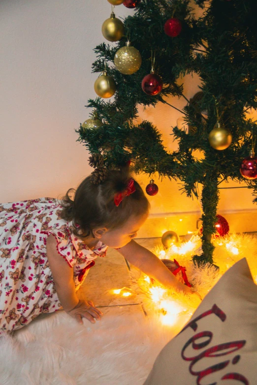 a little girl that is laying next to a christmas tree