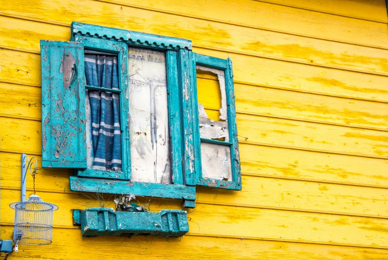 the window is open above the curtains on the yellow house