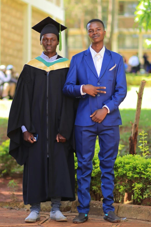 two men pose in front of a building in their graduation robes